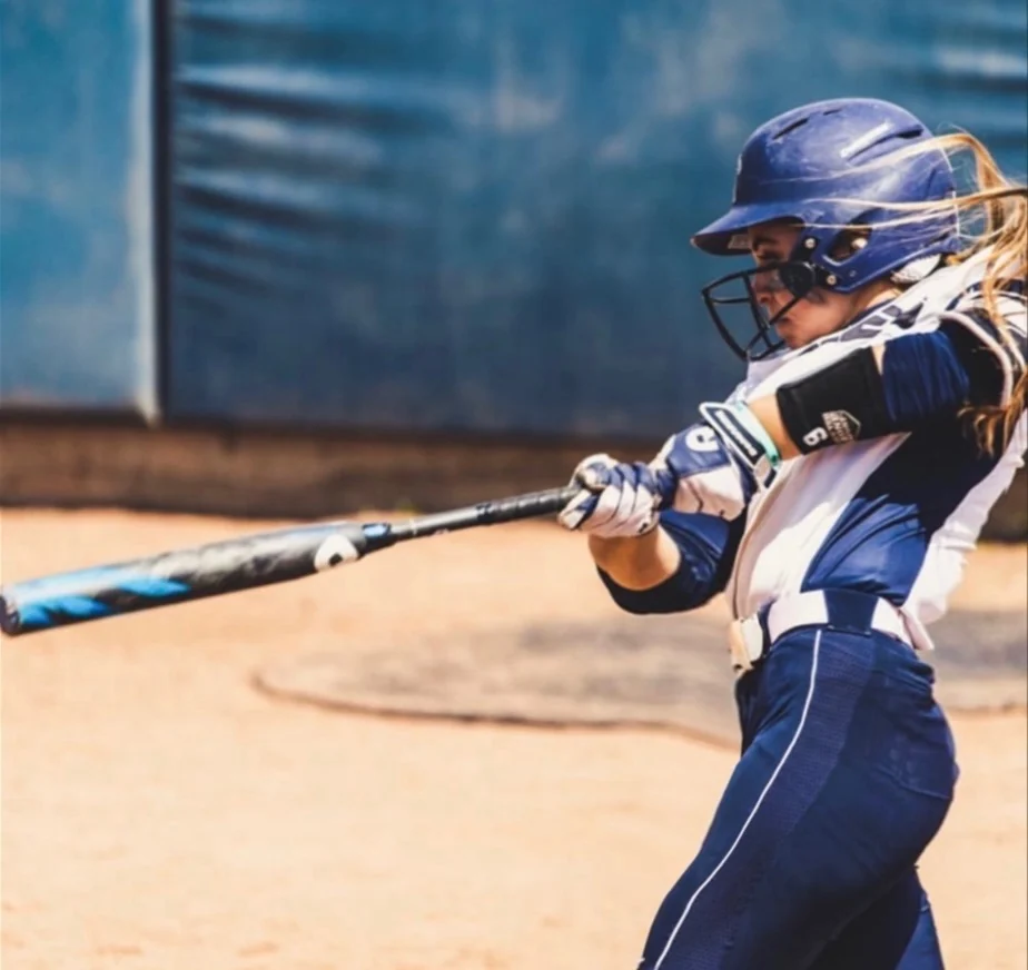 Softball hitter following through on a swing in a navy and white uniform
